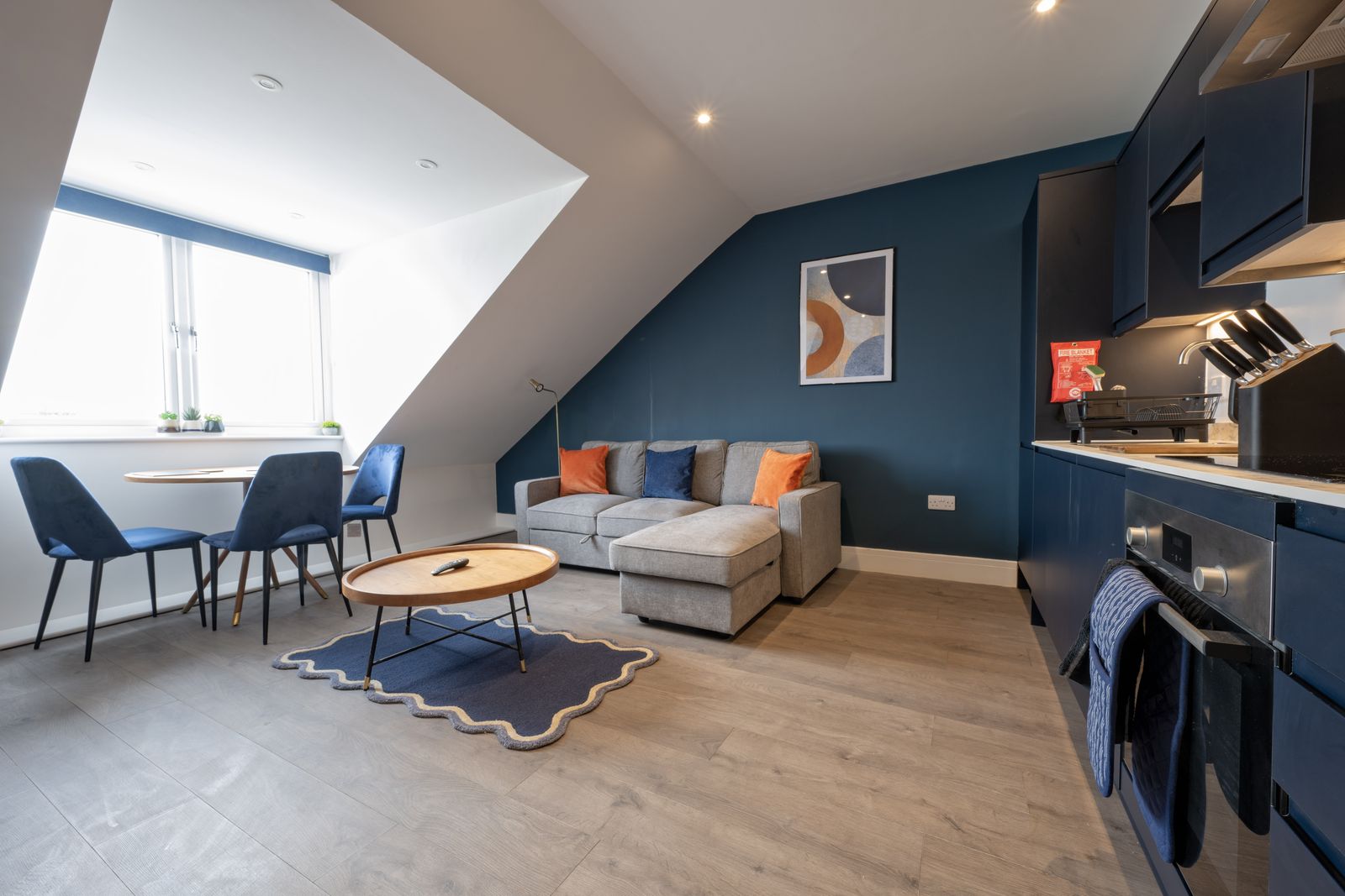 Open-plan living room and kitchen with sofa, dining table and navy walls
